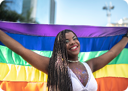 A woman smiling and holding an LGBTQ+ flag.