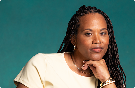 A black woman resting her chin on her hand looks at the camera with a slight smile.
