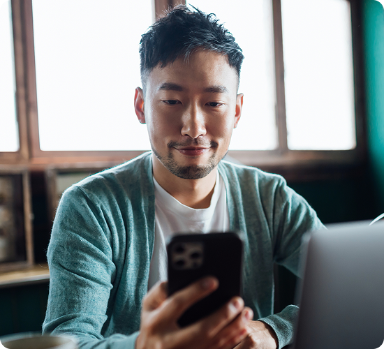 A person looking at a phone while sitting with a laptop.